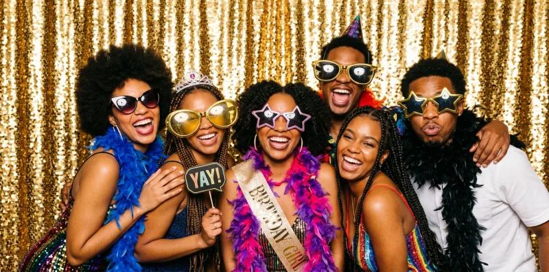 Groupe d'amis avec accessoires de fête devant un fond à paillettes dorées