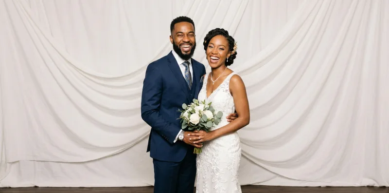 Couple de mariés posant devant la borne photo, sur fond drapé blanc