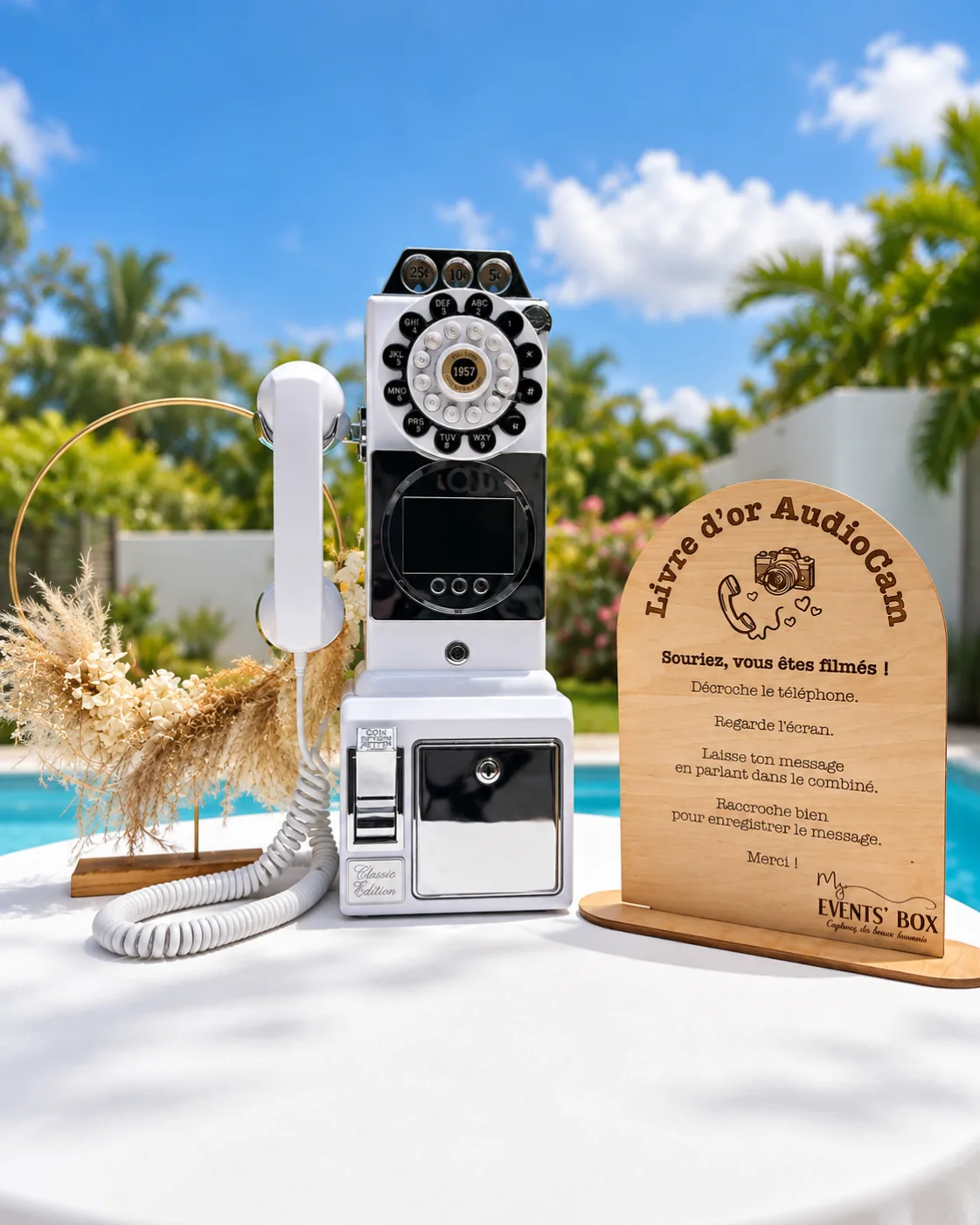 Téléphone vintage blanc à écran vidéo du livre d'or AudioCam et son chevalet en bois, sur une table au bord d'une piscine
