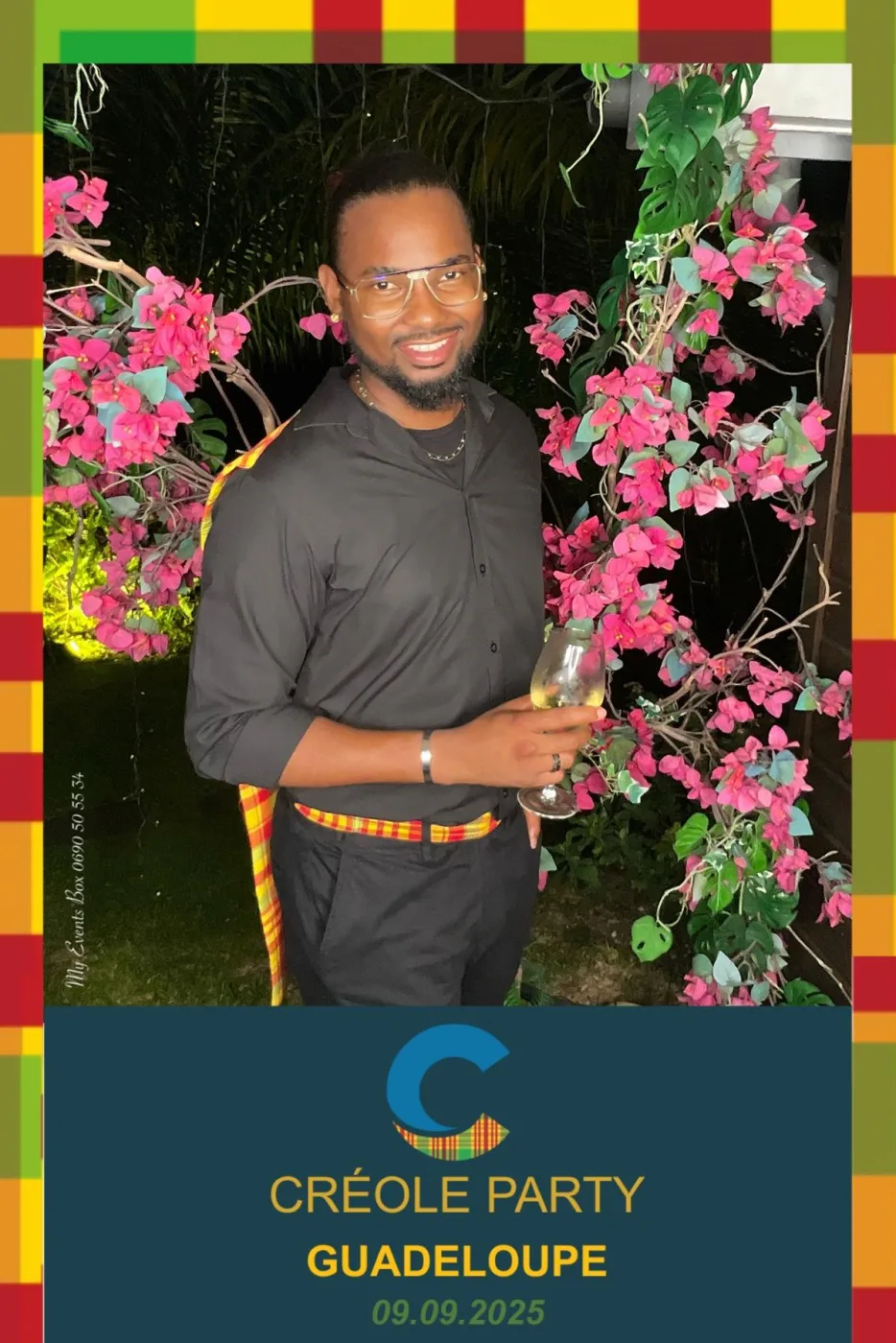 Tirage vertical au cadre madras pour une soirée créole : un invité en chemise noire et ceinture madras pose, verre à la main, devant des bougainvilliers en fleurs