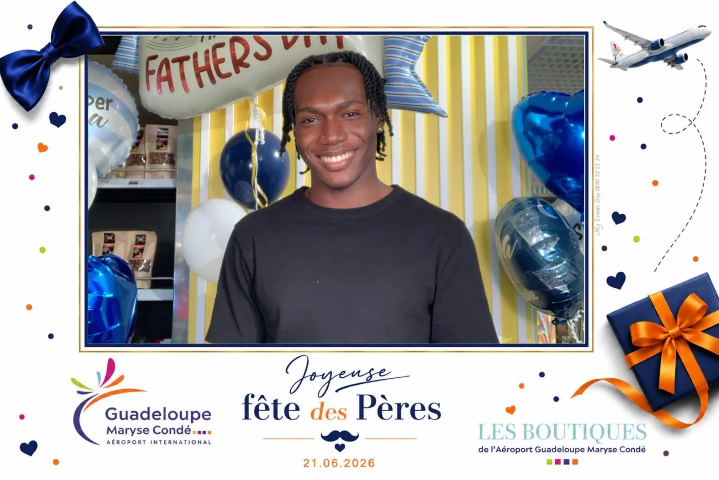 Cadre blanc à confettis, nœud papillon et coffret bleu nuit pour la fête des Pères aux boutiques de l'aéroport Guadeloupe Maryse Condé : un jeune homme pose devant un décor de ballons bleus et jaunes