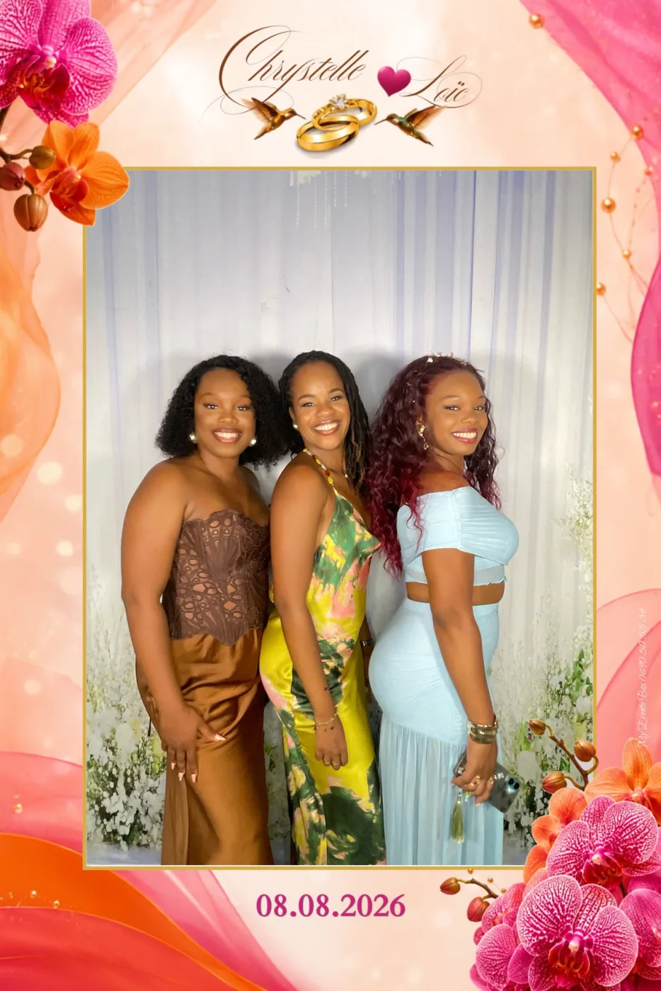 Tirage de mariage vertical : trois invitées en robes colorées devant le mur floral de la borne photo