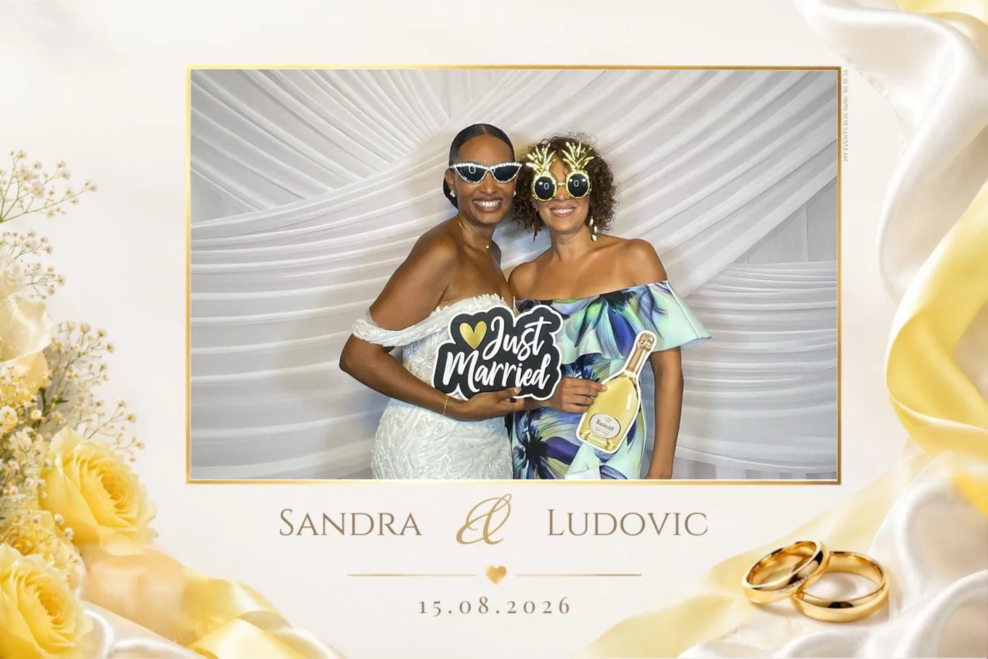 Tirage de mariage ivoire et or orné de roses jaunes et d'alliances : la mariée et une invitée posent avec lunettes fantaisie et pancarte « Just Married » devant le drapé blanc