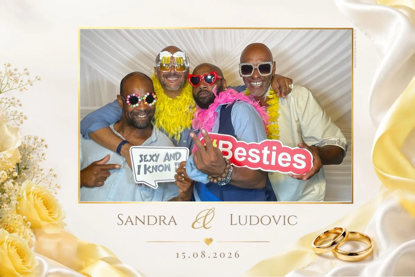 Tirage de mariage ivoire et or aux roses jaunes : quatre invités posent avec boas colorés, lunettes fantaisie et pancarte « Besties » devant le drapé blanc