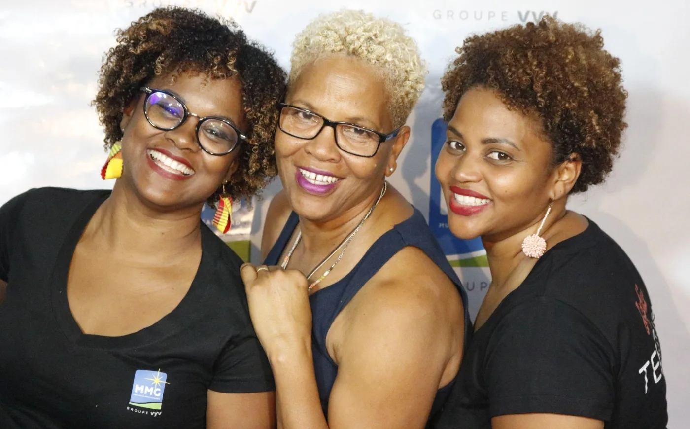 Trois femmes souriantes posées joue contre joue devant le fond photo d'un événement d'entreprise
