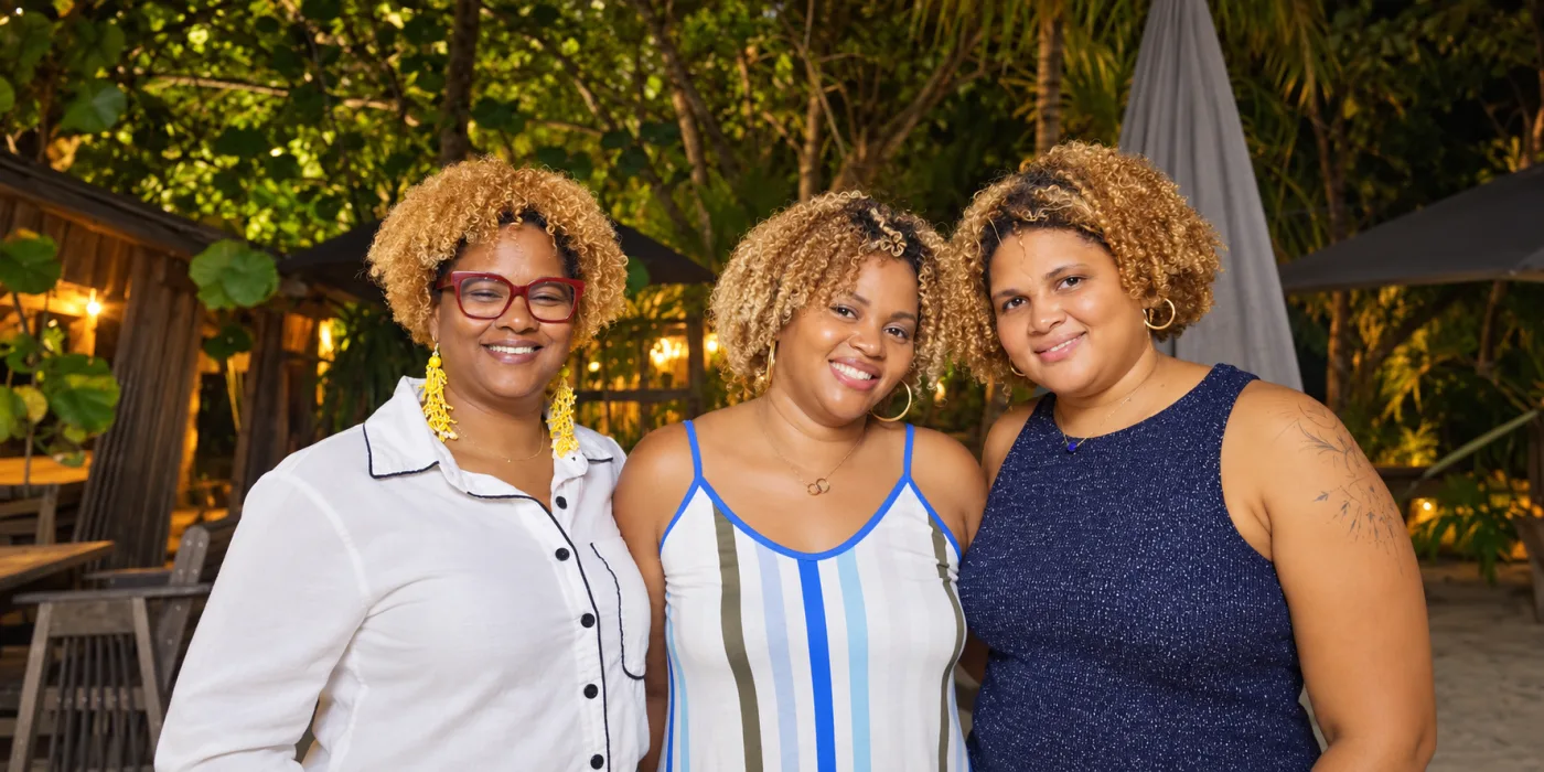 Trois femmes posent épaule contre épaule lors d'une soirée en extérieur, sous les lumières d'un jardin tropical